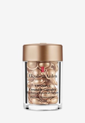 Klar cylindrisk beholder med et guld låg, fyldt med små, gyldne, kapsel-formede serum, mærket "Vitamin C Ceramide Capsules."