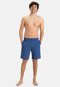 Modré krátke plavky s textúrovanou tkaninou, dvoma bočnými vreckami a predným zapínaním na gombík, s klasickým strihom a dĺžkou po kolená.