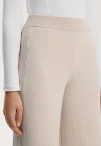 Ljust beige vida byxor gjorda av mjukt tyg med ribbad midja, med en slät yta och subtila sömdetaljer.