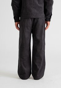 Black corduroy outfit featuring loose-fitting pants and a matching jacket. The fabric has a textured appearance with wide legs.