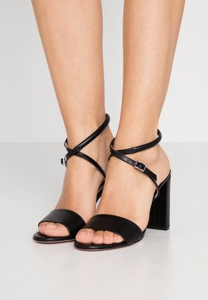 Sandalias de tacón negro con un acabado de cuero suave, diseño de punta abierta y finas correas para el tobillo sujetas con un hebilla. Detalle de tacón bloque.