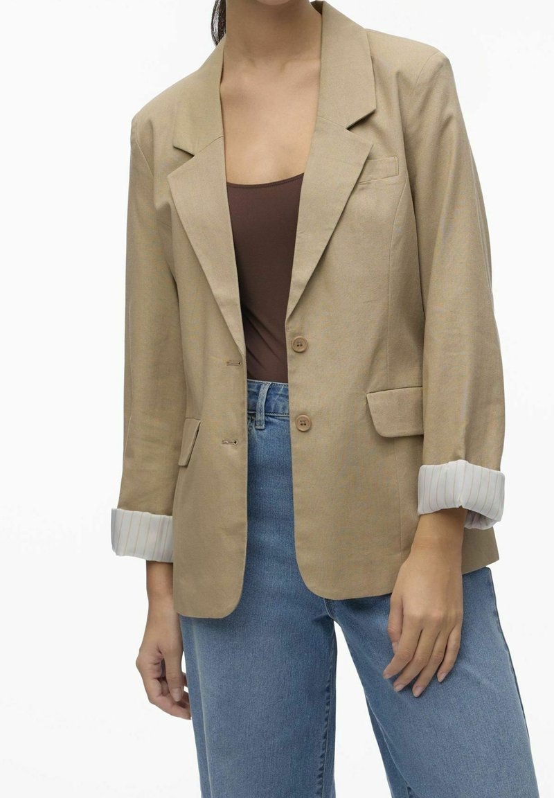 Beige blazer with notched lapels, two buttons, and front pockets. Cuffed sleeves with a white striped pattern. Paired with light blue jeans.