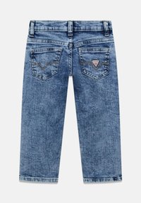 Jeans in denim blu con gambe dritte, due tasche posteriori e una piccola toppa triangolare con logo sulla tasca destra.