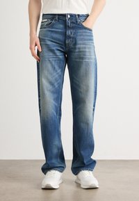 Modri denim traper hlače s ravnim krojem, ki vsebujejo detajle blatenja in obliko s petimi žepi. Uparjene z belimi supergami za kontrast.