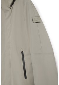 Chaqueta gris claro hecha de tela suave que presenta un bolsillo con cremallera negro y un parche rectangular "POLO CLUB" en el hombro.