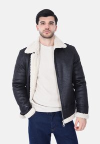 Giubbotto di pelle nera con un morbido rivestimento in shearling color crema e colletto. Presenta una chiusura con zip e polsini a costine, abbinato a un maglione leggero.