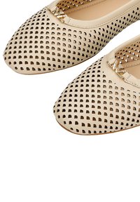 Ballerine beige perforate con punta arrotondata, caratterizzate da un accento dorato sul davanti e una superficie liscia. La suola mostrata è piatta.