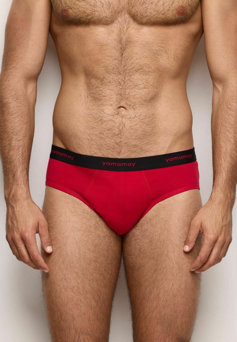 Rote Shorts aus weichem Stoff, mit einem schwarzen Bund, der das rote "yamamay"-Logo trägt. Enganliegendes Design mit minimaler Bedeckung.