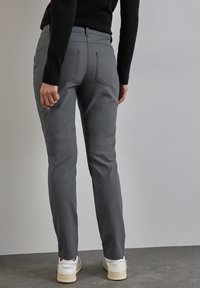 Grijze broek van gladde stof, met een getailleerd ontwerp, achterzakken en gecombineerd met witte sneakers. Achteraanzicht tegen een neutrale achtergrond.