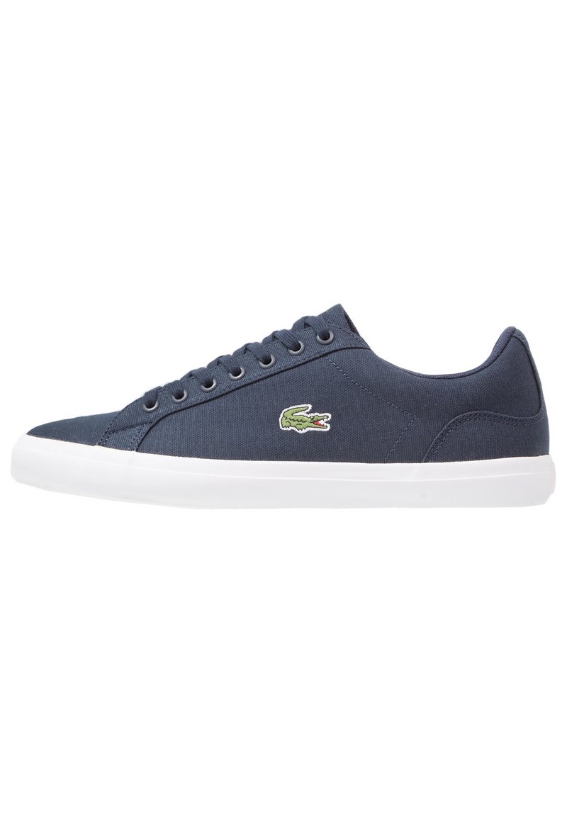 Baskets en toile bleu marine avec semelle blanche, lacets sur le devant, et logo crocodile vert sur le côté.