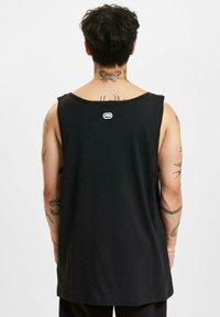 Black cotton tank top with a rounded neckline and a small logo at the back. The design features a loose fit and no sleeves.