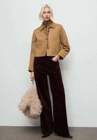 Corta chaqueta marrón con cuatro botones, blusa de cuello alto marrón, pantalones amplios burdeos y un bolso peludo rosa. Texturas suaves, diseño casual.