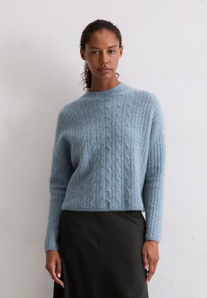 Light blue knitted sweater with a textured cable pattern and a rounded neckline. Paired with a black skirt, mid-length sleeves.