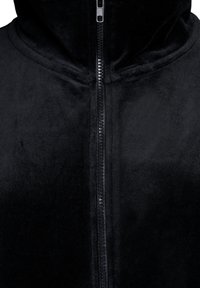 Svart zip-up jacka i mjuk, plyschig tyg. Har en hög krage och centralt dragkedja med strukturerad dragflik. Slät, jämn textur över hela. 