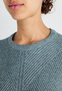 Pull côtelé texturé couleur sarcelle avec un col rond et des accents diagonaux. Tissu doux remarquable avec un éclat subtil.