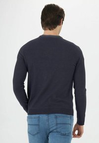 Marineblauer Strickpullover mit langen Ärmeln und geripptem Ausschnitt, kombiniert mit hellblauen Denim-Jeans. Der Stoff wirkt glatt und hat eine figurbetonte Passform.