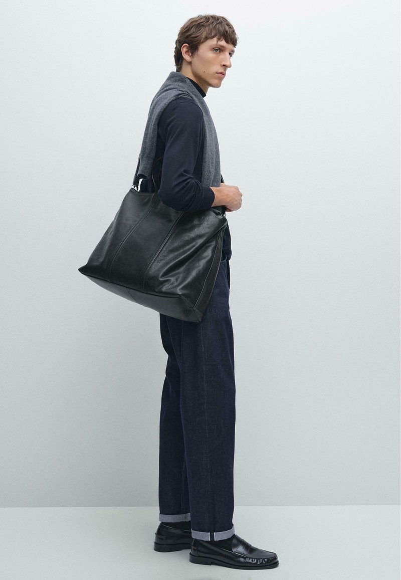 Czarna skórzana torba na ramię o gładkiej fakturze, prostokątnym kształcie i dwóch górnych uchwytach, wykończona prostym przeszyciem i bez widocznych elementów metalowych.