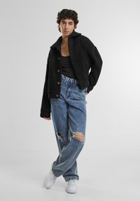 Zwarte nep-bontjas met grote kraag en knopen, gecombineerd met hoge, versleten blauwe jeans en witte sneakers.