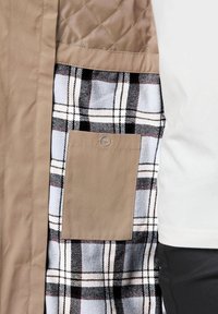 Beige buitenstof met een gestikte patroon; aan de binnenkant bevindt zich een zwart-wit geruite voering en een tan zak met een knoopdetail.