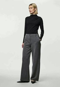 Top de manga longa preto com golas altas combinado com calças cinzas listradas de cintura alta e pernas largas. As calças possuem dois bolsos frontais. Sapatos pretos de bico fino.