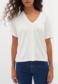 Vit V-ringad t-shirt i mjukt tyg, med korta ärmar och avslappnad passform, tillsammans med mörkblå jeans.