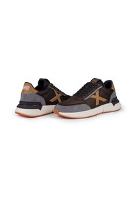 Hnědé a šedé tenisky s texturou z prodyšné síťoviny a semiše. Mají bílou podrážku, oranžový akcent a černé tkaničky. Logo na jazyku a na patě.