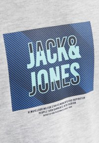 Grå bomulds t-shirt med et blåt og sort stribet rektangulært grafik med teksten "JACK & JONES" og mindre tekst under.