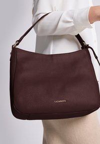 Borsa a tracolla in pelle bordeaux con finitura testurizzata, caratterizzata da un logo dorato, una silhouette curvata e una tasca a spalla.