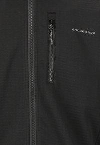 Svart jacka med frontdragkedja, utrustad med en bröstficka och "ENDURANCE"-logotyp. Slät textur och enkel design.