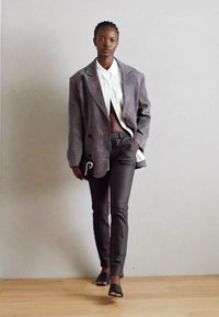 Grauer übergroßer Blazer, weißes Hemd, schwarze Hose und schwarze Rutsch-Sandalen; glatte Texturen und maßgeschneiderte Passform; dezente Verschlussdetails an der Hose.