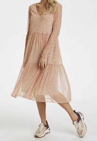 Rosarutigt långärmad klänning med V-ringning, lagerdesign och lätt genomskinlig textur, kombinerat med beige och vinröda sneakers.