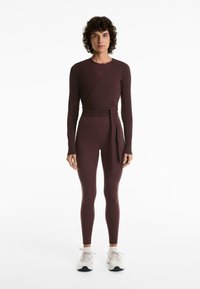 Burgundy, két részes sportos öltözet, amely hosszú ujjú, átkötős felsőből és magas derekú leggingsből áll, rugalmas, sima anyagból készült.