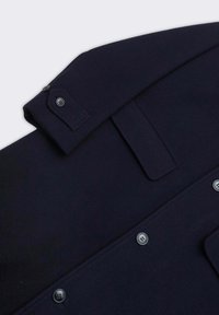 Cappotto in lana blu navy con polsini abbottonati, collo piatto e una texture liscia; presenta una patta con bottoni in metallo e un design pulito e su misura.