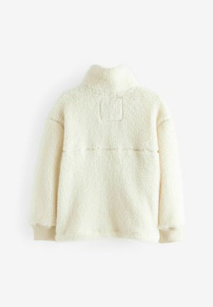 Kermanvärinen fleece-pullover, jossa on korkea kaulus, ribbikuidut, ja suorakulmainen merkki selässä; pehmeä rakenne kauttaaltaan.