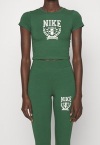 Osoba v odpovídajícím zeleném zkráceném tričku Nike a legínách s bílým logem Oregon 1972 na hrudi a stehně.