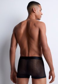 Boxer shorts noirs en matériau semi-transparent avec un motif géométrique. Dotés d'une ceinture noire lisse et d'un design ajusté.