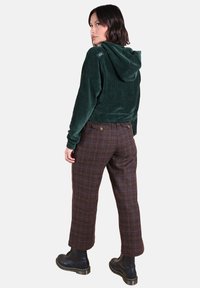 Hoodie en velours côtelé vert avec capuche, associé à un pantalon à carreaux marron doté d'accents bleus et de poignets retroussés. Bottes noires à lacets visibles.