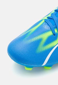 Botín de fútbol azul con parte superior sintética texturizada, que cuenta con acentos en verde neón y detalles en blanco, diseñado para el agarre y el rendimiento.