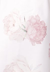 Biała tkanina z dwoma dużymi różowymi kwiatami piwonii z delikatnymi detalami, zielonymi liśćmi i subtelnie nadrukowanym napisem: „Le Brate.”