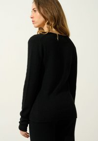 Czarny sweter wykonany z miękkiego materiału, charakteryzujący się luźnym krojem, długimi rękawami i lekko wyciętym dekoltem. Prosty i minimalistyczny design.