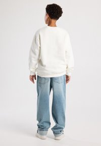 Sudadera blanca de cuello redondo con hombros caídos, combinada con jeans de corte suelto en azul claro que cuentan con bolsillos traseros y dobladillo deshilachado.