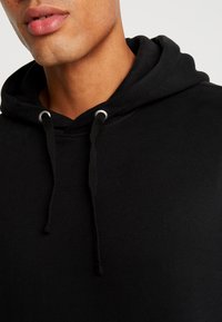 Schwarzer Kapuzenpullover aus weichem Stoff mit einer vorderen Kängurutasche, Zugbändern mit Metallspitzen und gerippten Bündchen.