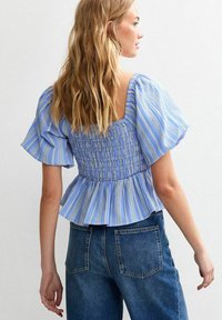 Blue and white striped top with puff sleeves, smocked bodice, and a flared peplum hem. Paired with high-waisted dark denim jeans.
