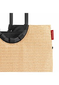 Sac en jute tissé avec des poignées noires, présentant une forme rectangulaire et une surface texturée. Comprend une étiquette rouge.