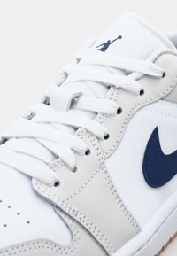 Nike teniske z belim usnjem in sivimi detajli, mornarsko modrim swooshom in belimi vezalkami. Teksturirana gumijasta podplati za boljši oprijem.