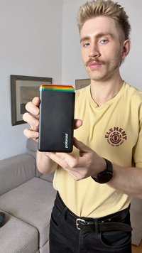 Polaroid bærbar skriver med en mat sort finish og en flerfarget stripe på toppen. Kompakt form, har merkevare på forsiden.