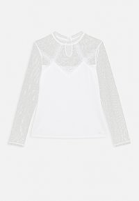 Top bianco a maniche lunghe con un corpo in tinta unita e maniche in tessuto traslucido a pois. Dettaglio a chiave sul retro con scollatura rotonda.