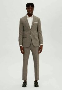 Traje de cuadros gris claro con un blazer ajustado y pantalones entallados; combinado con una camisa blanca y zapatos negros. Tejido texturizado, solapa afilada.