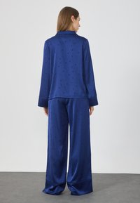 Set di pigiama in satin blu navy con un sottile motivo di stelle e lune crescenti; comprende una maglietta a maniche lunghe e pantaloni a gamba larga.