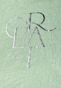 Světlá zelená látka s texturovaným tiskem v metalické stříbrné barvě, na které je zobrazeno slovo "SKVĚLÝ" a "a Barevný" v hravé typografii.